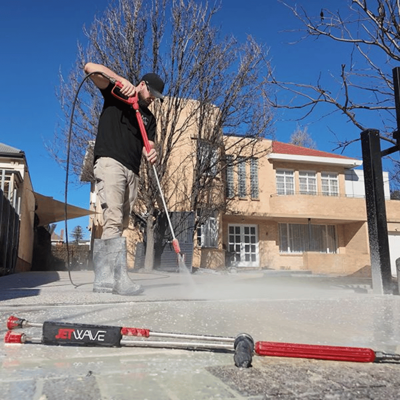 Person using a pressure washer on steps with a building in the background