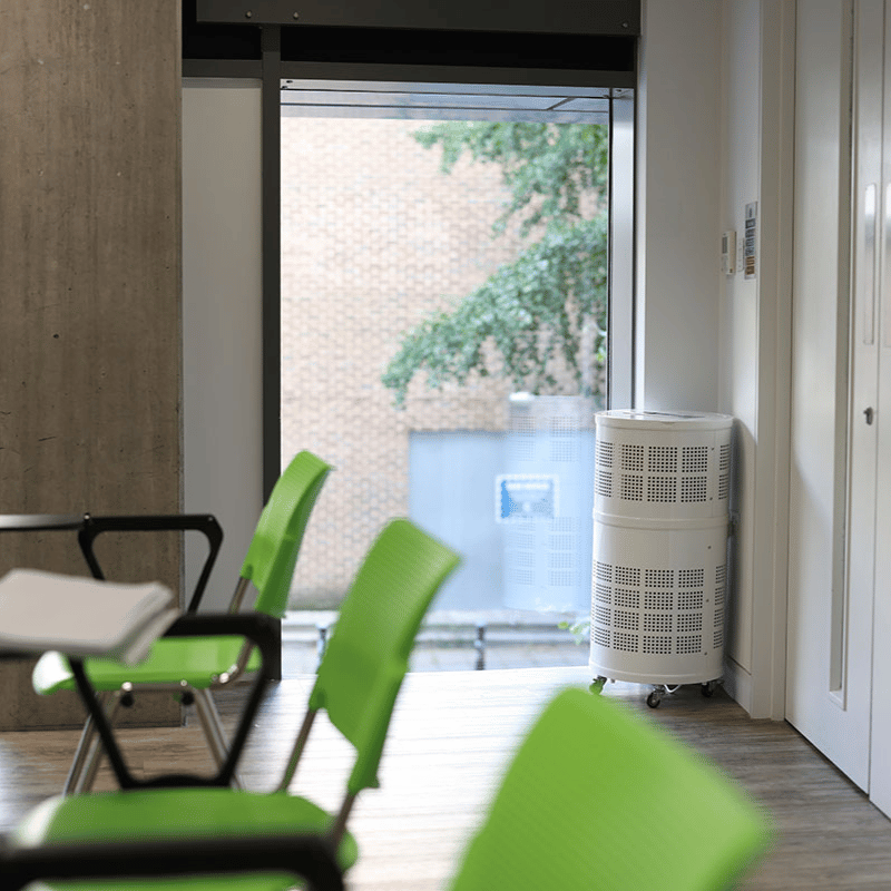 Rensair Air Purifier in commercial environment meeting room with green chairs and in the corner against a window. 