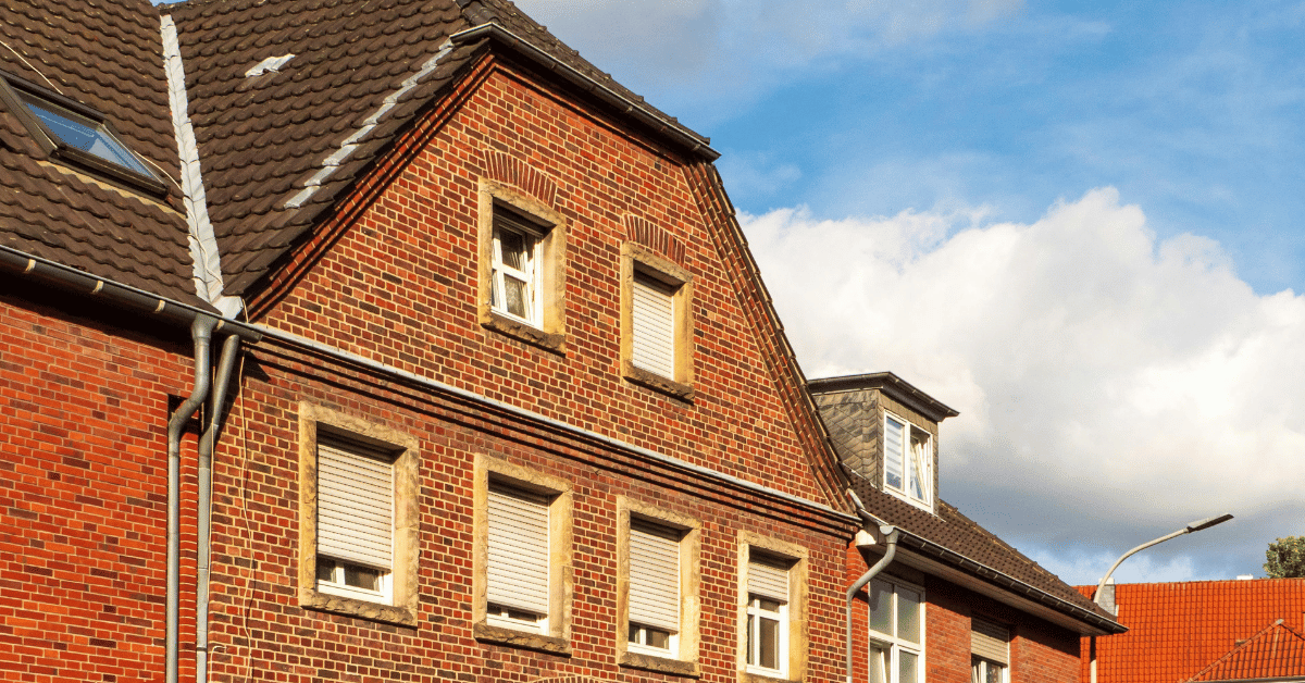 a red brick high set house with gutters and blue sky and clouds in the background