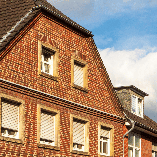 a red brick high set house with gutters and blue sky and clouds in the background