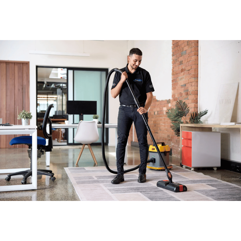 Person cleaning a carpeted office floor with a Cleanstar AS5 15L Commercial Plastic Dry Vacuum Cleaner and an activ8 powered floor tool 