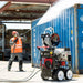 Worker in safety gear pressure washing a blue shipping container using a Jetwave Senator G2 275-20 Cold Water Petrol Pressure Cleaner with a hose reel.