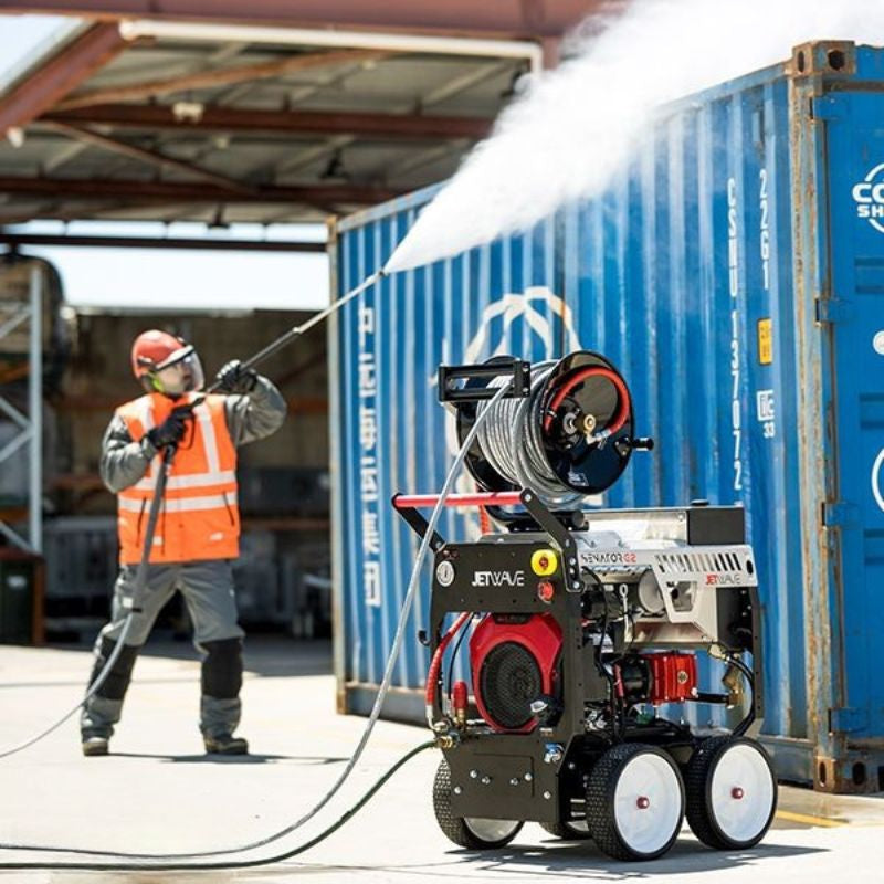 Worker in safety gear pressure washing a blue shipping container using a Jetwave Senator G2 275-20 Cold Water Petrol Pressure Cleaner with a hose reel.