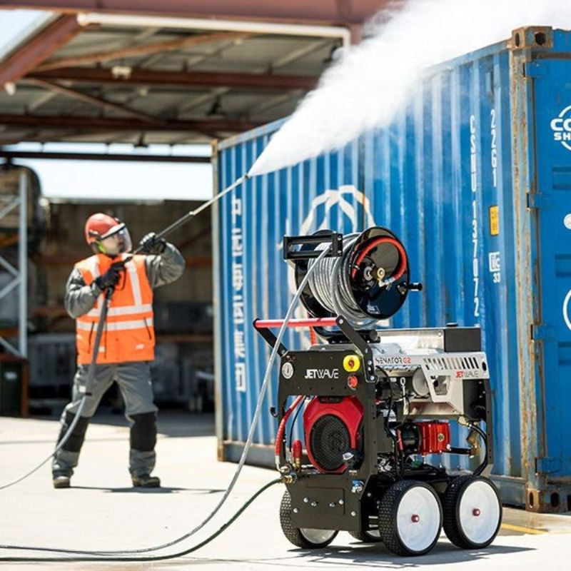 Worker pressure washing a blue shipping container using a Jetwave pressure cleaner with a hose reel.
