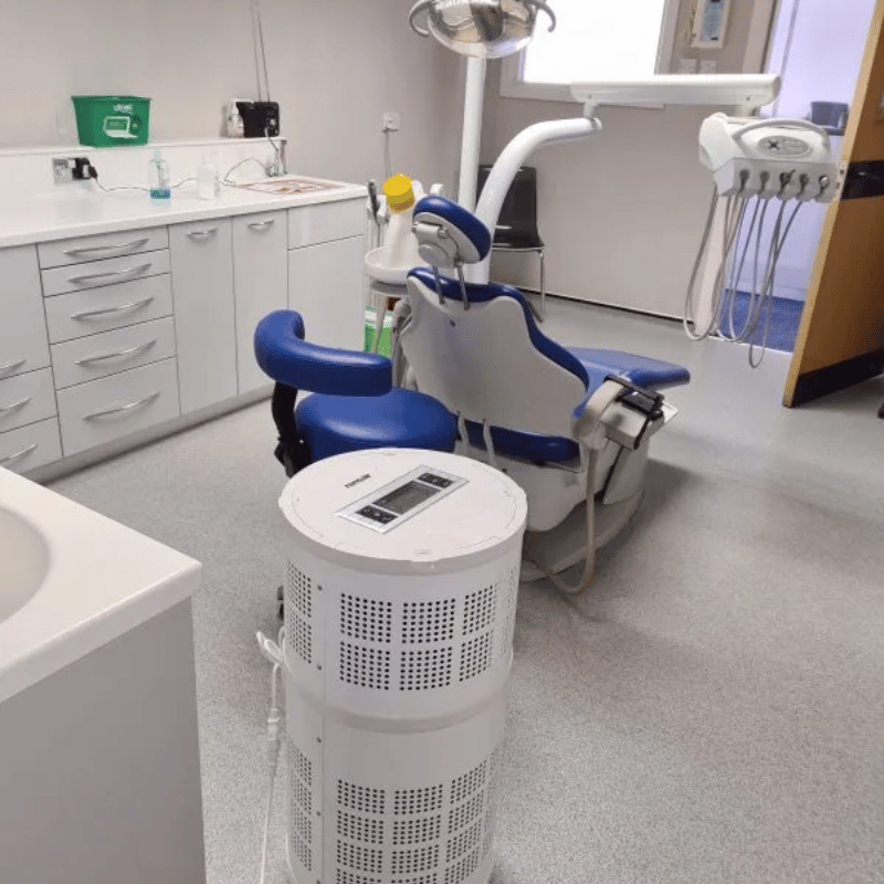 Dental office with a blue patient chair and Rensair air purifier on the floor.