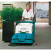 Person operating a Tennant 3640 Walk Behind Floor Sweeper in an indoor setting with a plant and window view.