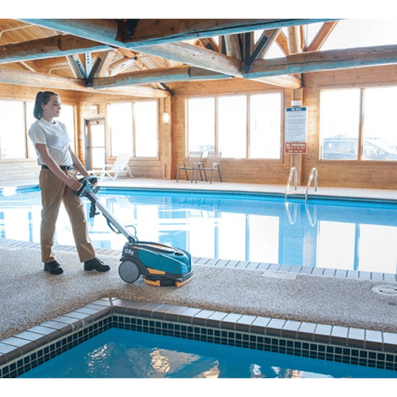 Person using a Tennant CS5 Micro Floor Scrubber by an indoor pool.