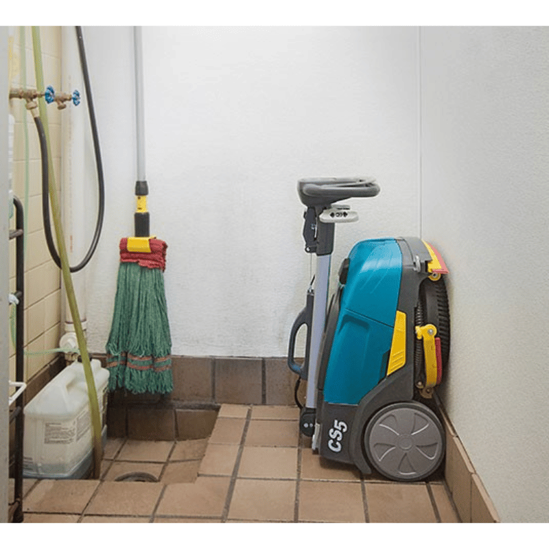 Cleaning equipment including a mop, pressure washer, and Tennant CS5 Micro Floor Scrubber in a bathroom.