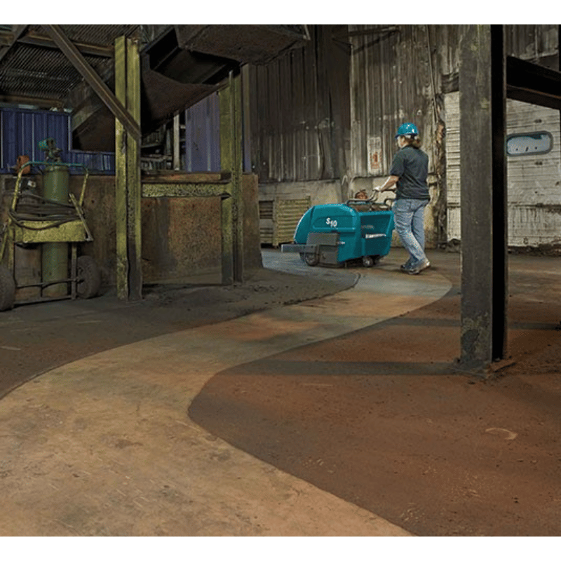 Person using a Tennant S10 Battery Walk Behind Floor Sweeper in a warehouse setting