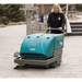 Person pushing a teal and gray Tennant S10 Battery Walk Behind Floor Sweeper on a paved surface.