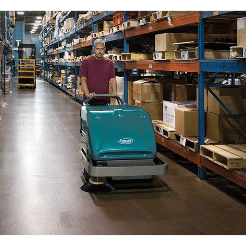 Man operating a Tennant S10 Battery Walk Behind Floor Sweeper in a warehouse setting