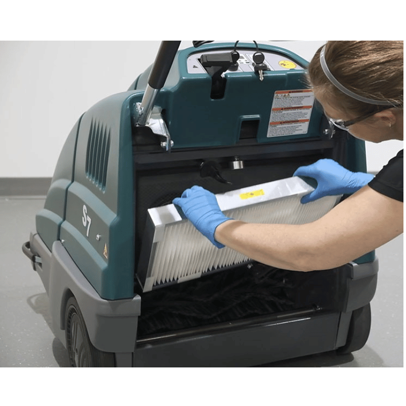 Person wearing gloves and a face shield cleaning a machine with a filter.