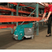 Man using a Tennant T1B Battery Compact Walk Behind Floor Scrubber to clean underneath a shelve in a warehouse facility.