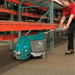 Person operating a teal floor cleaning machine in a warehouse setting