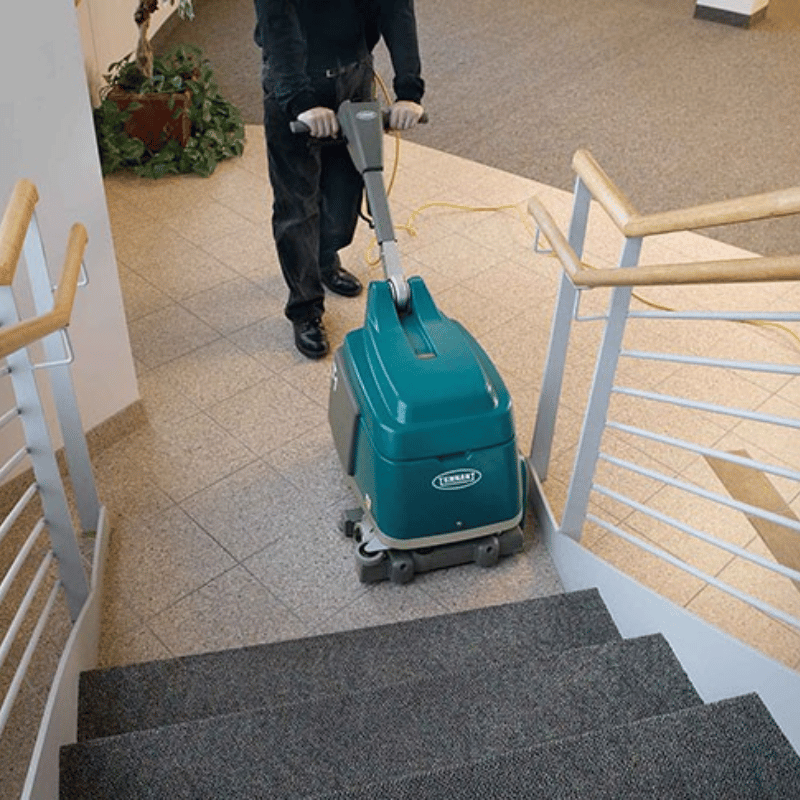 Person using a teal cleaning machine on a staircase in an indoor setting