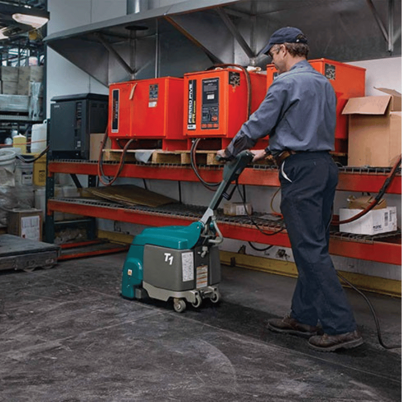 Person operating a teal machine in an industrial setting with red equipment in the background