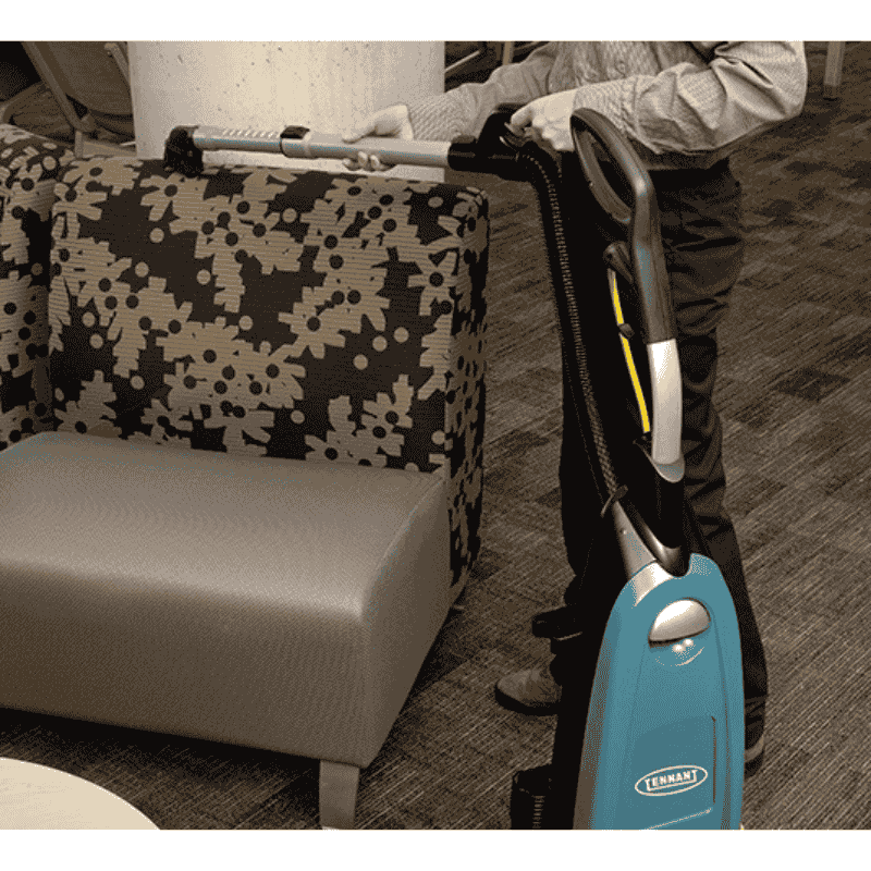 Person using a Tennant VSMU36 Upright Vacuum Cleaner on a patterned chair.