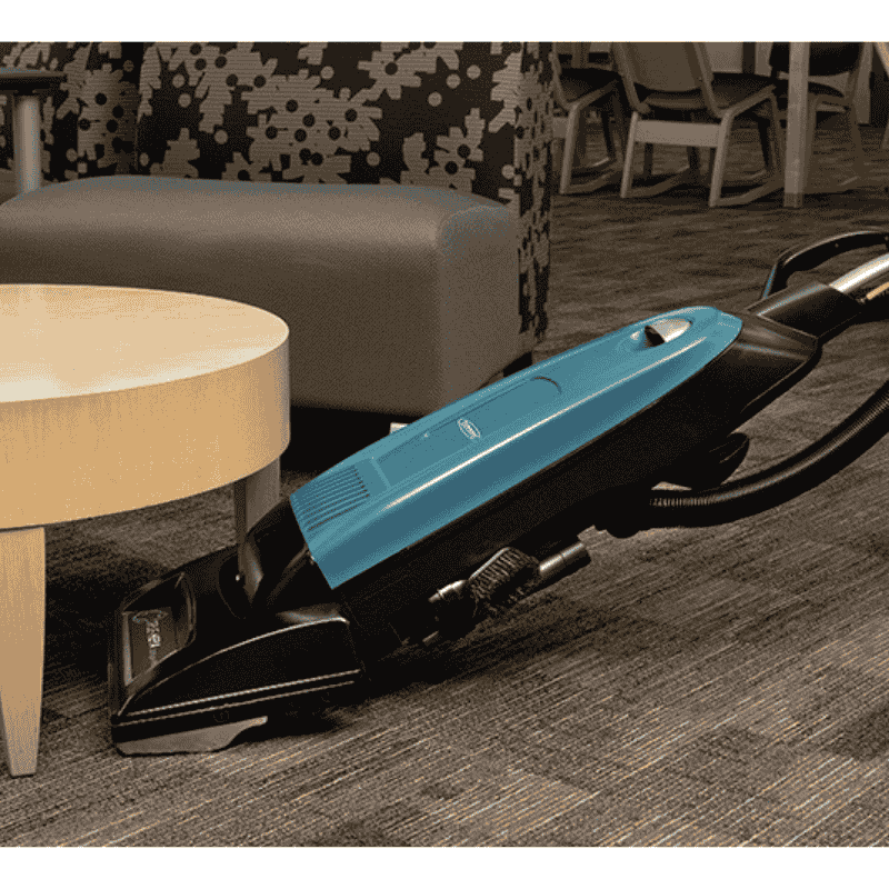 Tennant VSMU36 Upright Vacuum cleaning a carpeted floor in a living room setting underneath a coffee table
